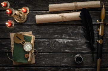 Adventure or travel concept background. Diary book of treasure hunter, golden compass, candle and ancient manuscripts on aged wooden table background with copy space.