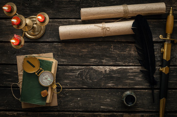 Adventure or travel concept background. Diary book of treasure hunter, golden compass, candle and ancient manuscripts on aged wooden table background with copy space.