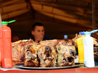 Three lamb heads chopped off from lambs previously roasted at a spit, on an iron tray. In a blurry...
