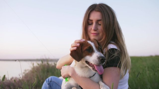 Young happy woman and het little dog sitting with flying kite on a glade at sunset