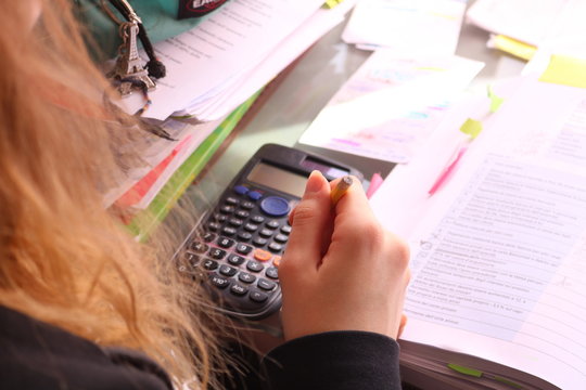 Young poor woman uses calculator on table with sheets. Bad financial situation