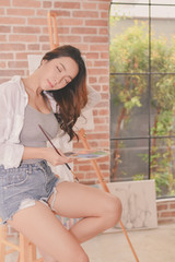 Fototapeta premium Concept Artist Beautiful girl. Beautiful women are creating art. Beautiful woman is painting happily. Young artist painting in the gallery.