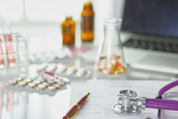 closeup of the desk of a doctors office with a stethoscope in the foreground and a bottle with pills in the background, selective focus