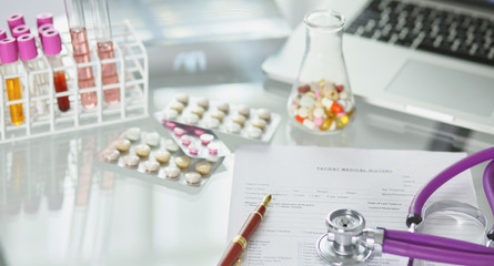 Obraz na płótnie Canvas closeup of the desk of a doctors office with a stethoscope in the foreground and a bottle with pills in the background, selective focus