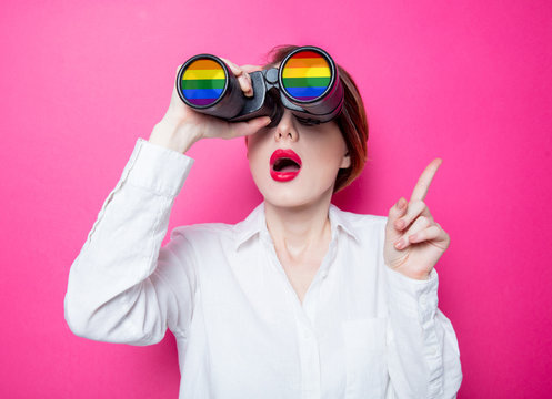 Beautiful redhead businesswoman with rainbow binoculars on pink background