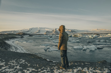 Young man staring at a frozen lagoon landscape at sunset