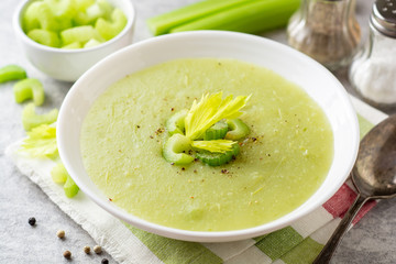 Celery cream soup in white plate on gray stone background