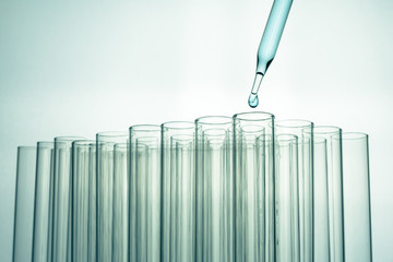 Pipette over laboratory test tube in rack dropping sample chemical for science experiment in lab