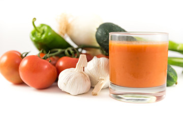 bunch of tomatoes, garlic, cucumbers, peppers, onions and a glass of tomato soup or gazpacho on white background