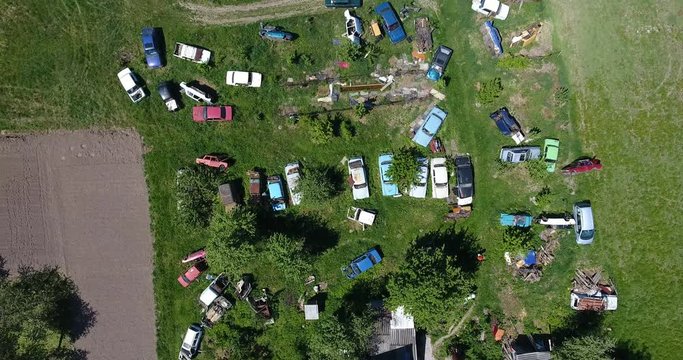 Aerial view of broken rusty cars amidst greenery, the field lined with old machines for disassemble
