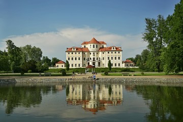Fototapeta na wymiar Liblice, Czech Republic / Europe - May Day Year: Reflection of castle Liblice close to Melnik in water built in baroque style with garden, gazebo,lake, green grass, trees, on a sunny day with blue sky