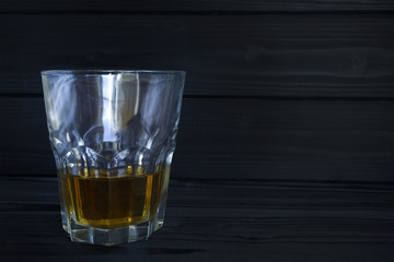 a glass with alcohol on a dark, woody background