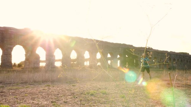 Young man in sportswear running along ancient roman aqueduct Appio Claudio. Training outdoor alone in peaceful park in Rome at sunset slow motion.