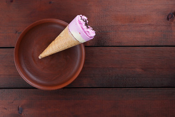 Yellow pink ice cream with chocolate in a waffle cup. Ice cream on a dark wooden background. Cold milk dessert on a clay plate. Copy space. Summer cold dessert