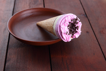 Yellow pink ice cream with chocolate in a waffle cup. Ice cream on a dark wooden background. Cold milk dessert on a clay plate. Copy space. Summer cold dessert