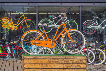 An orange bicycle on a wooden pedestal, in the background of a bicycle rental shop window