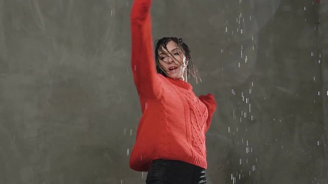 The girl dances in the rain. Wet female dancer in a red sweater circles around himself under the drops of rain. Modern dance