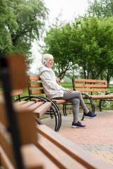 senior woman listening music in headphones on bench in park