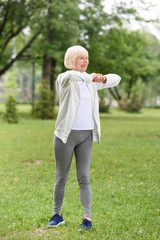 senior caucasian sportswoman exercising on green lawn in park