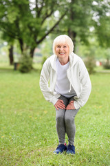 happy senior sportswoman squating on green lawn in park