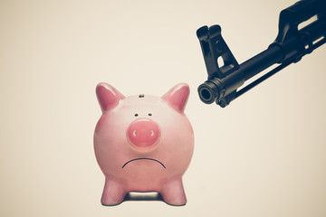 A rifle pointing at a pink piggy bank / Terrorism threatening economy concept