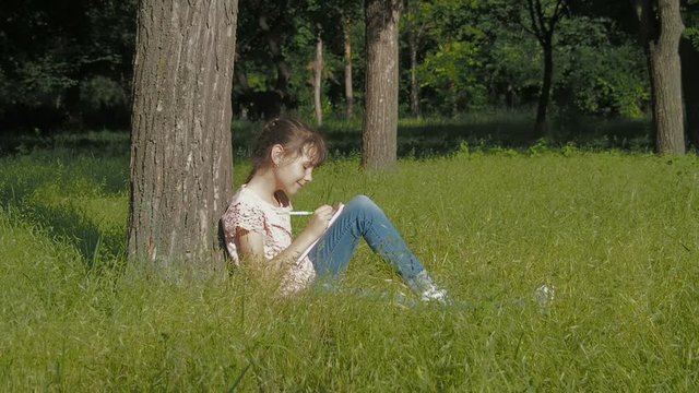 The child draws in the park. Little girl draws with pencils on nature.