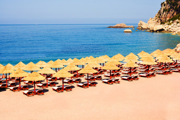 Obraz premium Beach Umbrella made of palm leafs on the background of an exotic beach in Montenegro. Relaxing area: sun beds in the shadow of rustic umbrella. Sea view