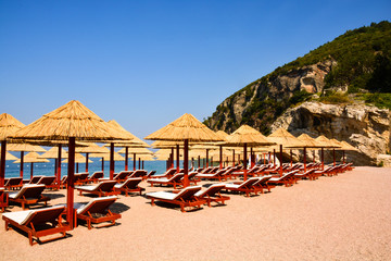 Beach Umbrella made of palm leafs on the background of an exotic beach in Montenegro. Relaxing area: sun beds in the shadow of rustic umbrella. Sea view