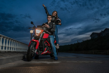 Fototapeta na wymiar Biker couple man and woman on a black and red color sport motorcycle. Night view