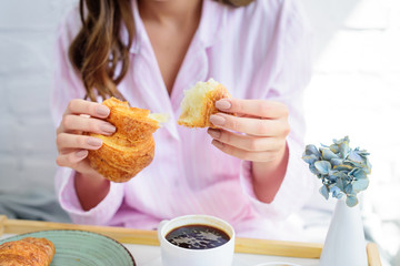 partial view of woman in pajamas having croissant and coffee for breakfast
