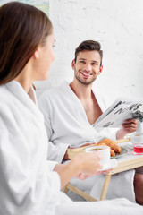 young family in bathrobes having breakfast and reading newspaper in bed