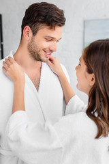 Naklejka premium happy couple in white bathrobes standing together in morning