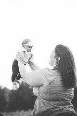 Happy mother with baby having fun outdoors, joyful young mom lifting up her precious baby girl