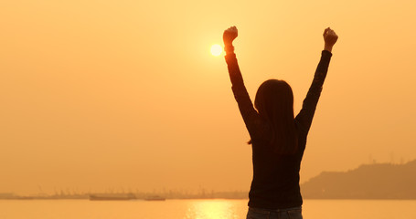 Woman raising hand up under sunset