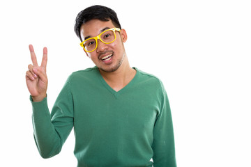 Studio shot of young happy Asian man smiling and giving peace si