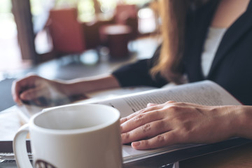 Closeup image of a business woman reading a book with coffee cup on table in cafe
