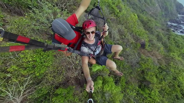 Two men flying on paraplane above cliff break and sea shore gopro selfie