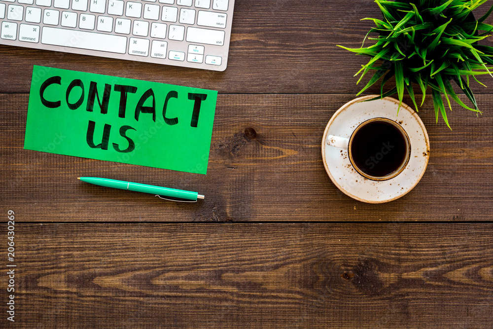 Poster frame contact us. lettering contact us on office work desk with computer on dark wooden background t