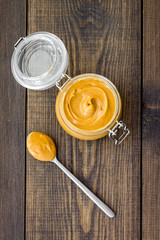 Nut butter in glass jar and spoon with butter on dark wooden background top view