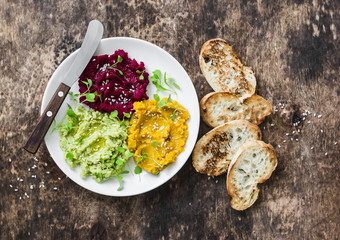 Pumpkin, turmeric, avocado, beetroot hummus with olive oil, sesame seeds and microgreens on a wooden background, top view. Delicious vegetarian snacks. Copy space