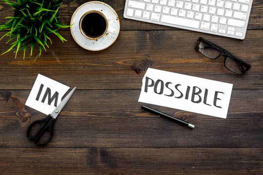 From impossible to possible. Do difficult task at work concept. Cutting the part im of written word impossible by sciccors. Office desk. Dark wooden background top view copy space