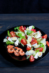 Mix salad with fresh vegetables and apetite shrimps in a black plate