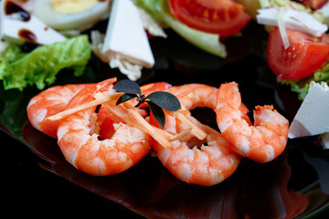 Mix salad with fresh vegetables and apetite shrimps in a black plate