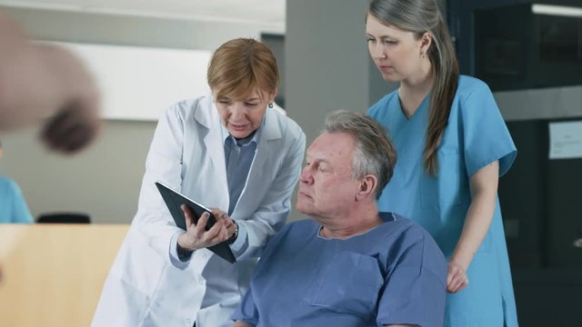 In the Hospital Female Doctor Shows Tablet Computer to Elderly Patient, Explaining his Condition. Modern Hospital with Best Possible Care. Shot on RED EPIC-W 8K Helium Cinema Camera.