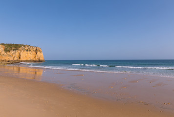 Atlantic beach at sunset during low tide. Waves are rolling on a sandy beach in Algarve, Portugal.