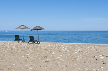 Beach chairs under thatched umbrellas with blue sea and sky on sunny summer day. A beautiful place to relax. Sunbeds on the beach against the azure or turquoise calm sea with boat