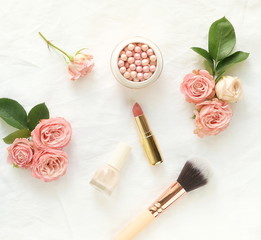 Obraz na płótnie Canvas Makeup cosmetic accessories products pearl make up powder and brush, lipstick, pale pink roses on white linen fabric background. Flat lay. Top view. Copy space