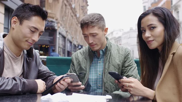 Young group of asian friends using their phones at a cafe table before smiling to camera 