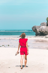 Girl in a red dress walking barefoot on the sea shore. Tropical beach, Bali island. Sunny day.