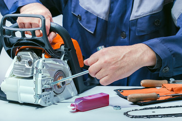 Professional technician working in repair service. Repairing chainsaw on workbench.